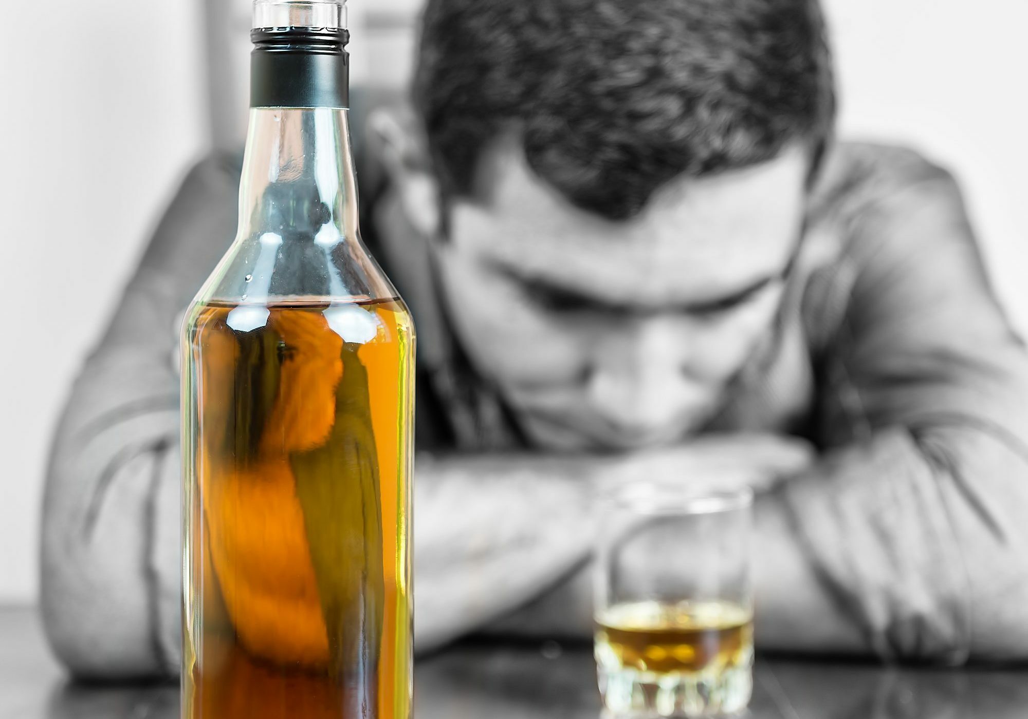 Whisky bottle with an out of focus drunk man in the background (only the bottle and the glass have color)